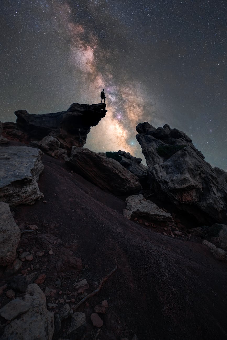a man standing on top of a rock with the milky in the sky